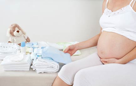 Heavily pregnant woman sitting on bed and fondling towels she will use after the baby is born